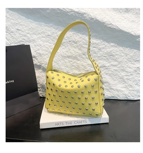 Detail of yellow pebbled leather handbag featuring dense silver rivet studs and top handle