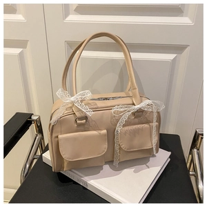 Detailed close-up of beige pillow handbag featuring lace bows and dual front pockets