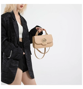 Detail of beige crossbody bag featuring a gold metal M logo buckle and adjustable strap