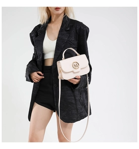 Detail view of cream crossbody bag with gold M letter clasp and top handle on blazer