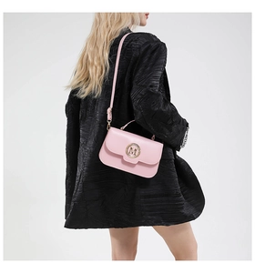 Close-up of pink crossbody bag with golden M buckle worn with an oversized black blazer