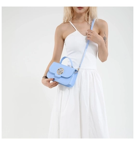 Sky blue crossbody bag with gold M buckle worn by model in white summer dress