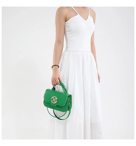 Detail of emerald green leather handbag with gold M logo on white summer dress