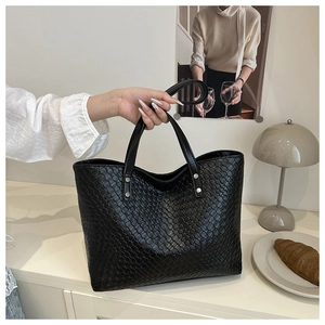 Detail of black woven leather tote bag featuring metal rivets and premium braided texture