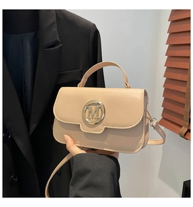 Detail of beige flap bag featuring a large gold letter M buckle and fixed top handle