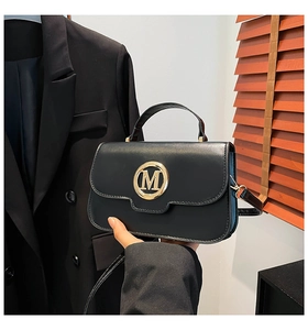 Detail of black matte leather handbag with gold M-letter buckle and adjustable strap