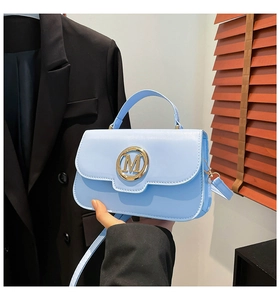 Detail shot of light blue crossbody bag with gold M logo on a smooth faux leather flap