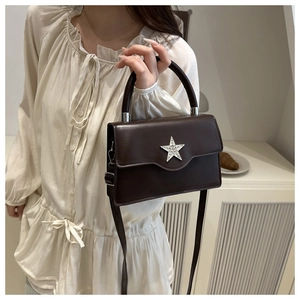 Détail d'un sac bandoulière marron foncé brillant avec un emblème étoile en strass