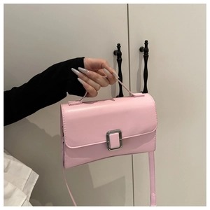 Vue détaillée d'un petit sac carré rose avec boucle en métal argenté tenu à la main