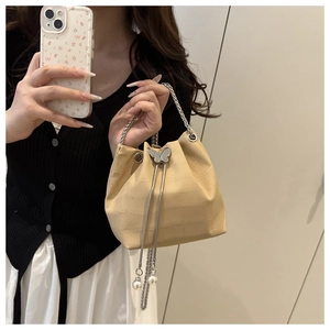 Detail of beige pleated bucket bag with crocodile texture, silver bow, and pearl charm