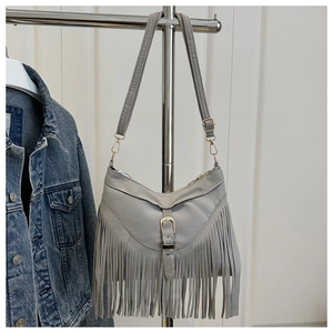 Detail of grey suede shoulder bag with long fringes and gold metal buckle on a rack