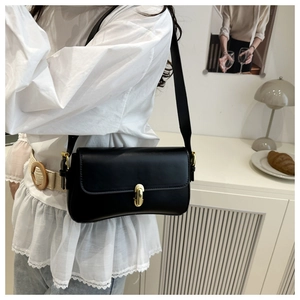 Minimalist black leather underarm bag with gold oval buckle shown on shoulder of a model