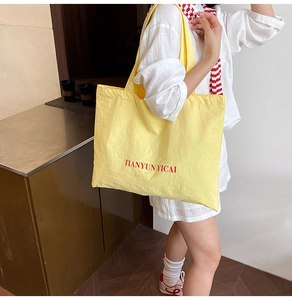 Détail d'un sac cabas en toile jaune à grande capacité avec impression de lettres rouges