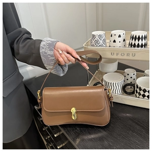 Detailed view of brown leather underarm bag with golden metallic twist lock and strap