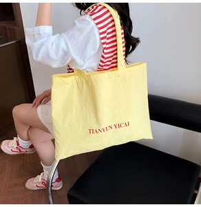 Détail d'un grand sac cabas en toile jaune avec lettres TIANYUN YICAI rouges et bandoulières