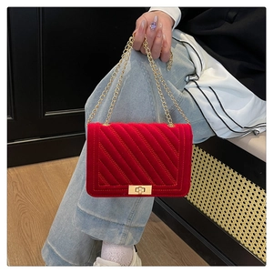 Détail d'un sac bandoulière en velours rouge matelassé avec chaîne dorée sur un mannequin