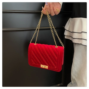 Détail du sac à bandoulière en velours rouge avec chaîne dorée et texture matelassée