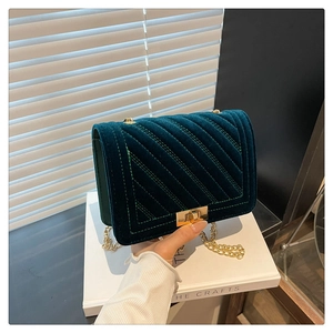 Détail du sac en velours vert foncé avec surpiqûres en V et chaîne en métal doré