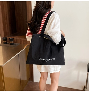 Détail d'un grand sac cabas en toile noire avec lettrage blanc TIANYUN YICAI sur l'épaule