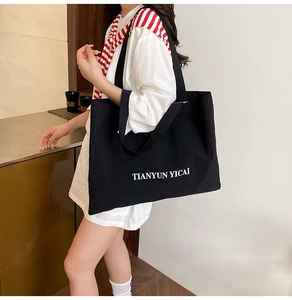 Vue latérale du grand sac cabas noir en toile avec lettrage blanc sur le mannequin