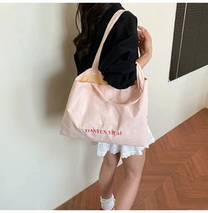 Sac fourre-tout en nylon rose avec lettrage rouge porté à l'épaule par un mannequin