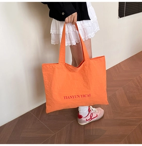 Détail d'un grand sac cabas en toile orange vif avec lettrage rouge dans un cadre décontracté