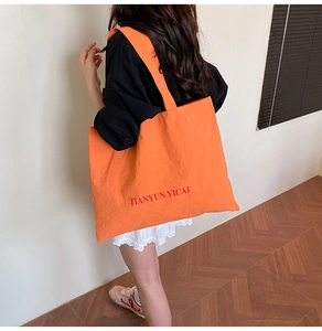 Vue latérale du grand cabas en toile orange avec logo rouge porté par un mannequin