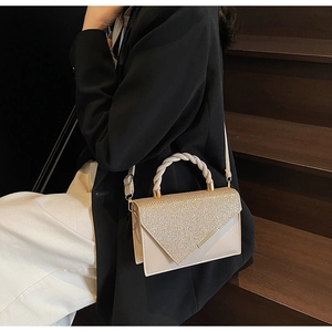 Detail of elegant beige square bag with gold shimmer, V-metal trim and pearl woven handle