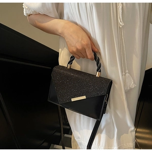 Detail of black crossbody bag with gold hardware and sparkling texture on white dress