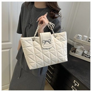Close-up of white quilted tote bag featuring silver bow clasp and chain strap