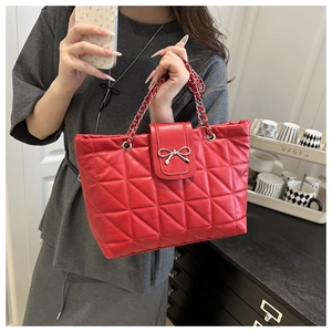 Detail of red quilted tote bag featuring silver bow metal decor and chain strap