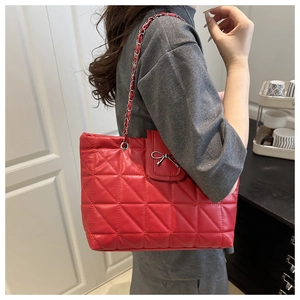 Détail du sac cabas matelassé rouge avec nœud argenté et bandoulière chaîne à l'épaule