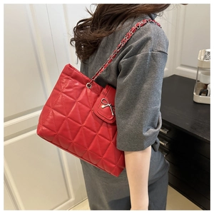 Detail of red quilted tote bag with metal chain strap and bow pocket shown on a model