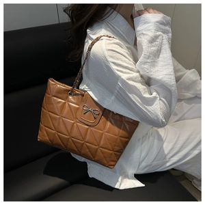 Detail of a brown quilted tote bag with a silver metal bow buckle and chain strap