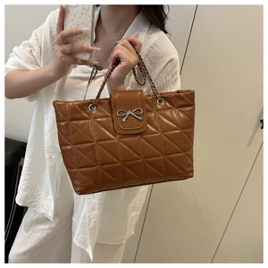 Detail of caramel quilted tote bag with silver bow ornament and chain strap detail