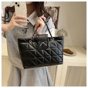 Detail of black quilted tote bag with silver bow ornament and chain shoulder strap