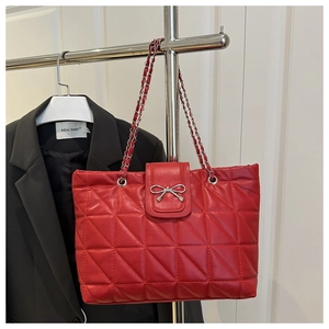 Close-up of red quilted tote bag with silver bow ornament and chain strap detail