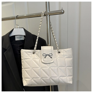 Detail of white quilted tote bag featuring silver bow accent and woven chain strap