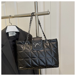 Close-up of black quilted shoulder bag with silver bow buckle and chain strap detail