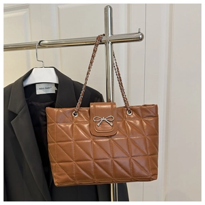 Detail of brown quilted leather tote featuring a silver bow clasp and chain strap