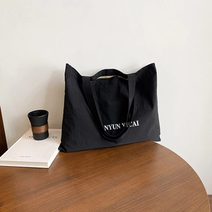 Sac fourre-tout noir minimaliste en toile avec lettrage blanc sur une table en bois