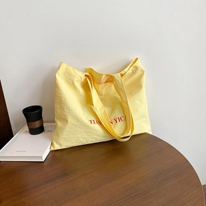 Sac fourre-tout minimaliste jaune pâle avec lettrage rouge sur table en bois