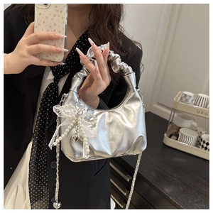 Detail of silver metallic pleated handbag with pearl lace bow and heart pendant