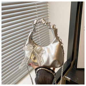 Detail of silver metallic hobo bag featuring ruched handle and pearl bow charm with chain
