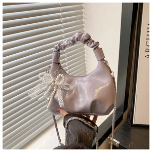 Detail of lavender pleated handbag featuring pearl bow lace charm and chain strap