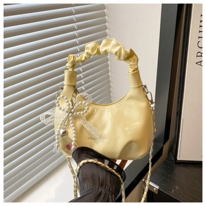 Detail of pale yellow pleated handbag with pearl bow charm and golden chain strap