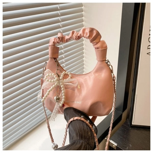 Detail of pink pleated crescent bag featuring pearl bow charm and lace trim accents