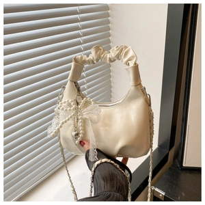 Detail of cream white crescent bag featuring pleated handle and pearl lace bow charm