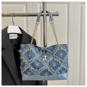 Detail of blue denim tote featuring star prints, frayed edges, and golden deer charm