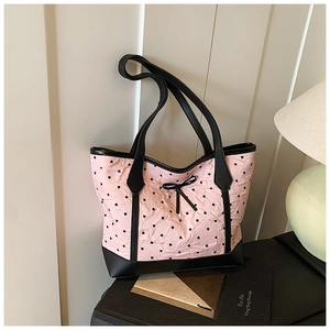 Detail of pink heart-patterned tote bag featuring black leather trim and bow accent